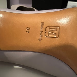 May include: Close-up of the bottom of a light purple shoe with a brown leather sole. The sole is stamped with the text "Made in Italy" and the letter "M" in a square. The size 37 is also visible.