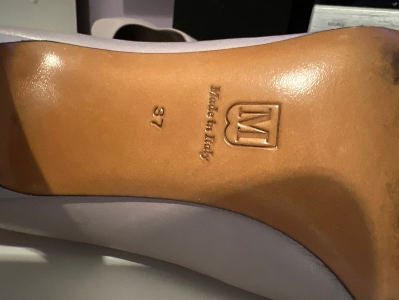 May include: Close-up of the bottom of a light purple shoe with a brown leather sole. The sole is stamped with the text "Made in Italy" and the letter "M" in a square. The size 37 is also visible.