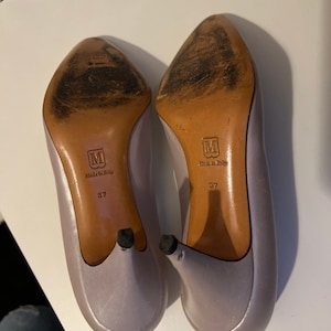 May include: A pair of lavender satin heels with a pointed toe and a stiletto heel. The heels are size 37 and say "Made in Italy" on the bottom.