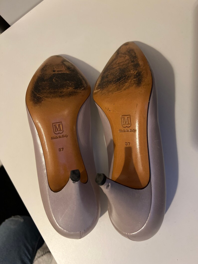 May include: A pair of lavender satin heels with a pointed toe and a stiletto heel. The heels are size 37 and say "Made in Italy" on the bottom.