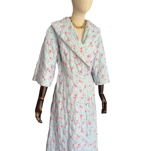 Peut inclure: Une robe de chambre matelassée bleu clair avec un motif floral rose. La robe a un col châle et une silhouette longue et fluide.