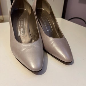 May include: A pair of silver leather pumps with pointed toes. The shoes have a small heel and are labeled "Bruno Magli" on the inside.