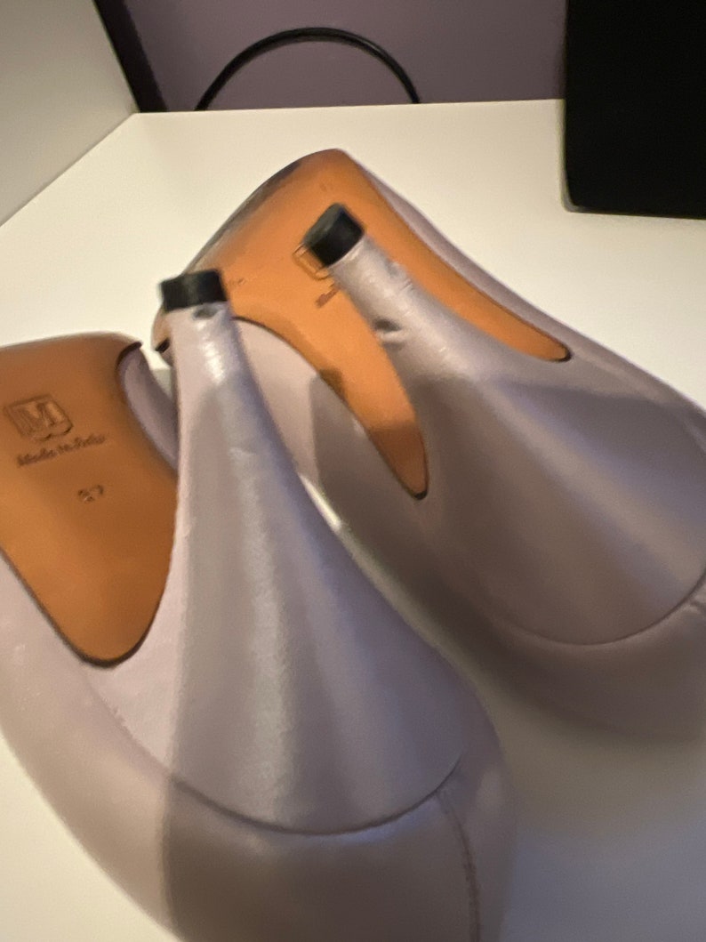 May include: A pair of light purple satin high heels with a pointed toe and a thin heel. The shoes are made in Italy.