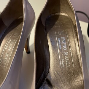 May include: A pair of gray leather pumps with a high heel. The inside of the shoe has a label that reads "Bruno Magli, Made in Italy, Bologna".