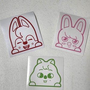 May include: Three cartoon animal stickers. One is red, featuring a smiling rabbit. Another is pink, depicting a bunny with a stern expression. The third is green, showing a hamster-like creature. All are on white backgrounds.