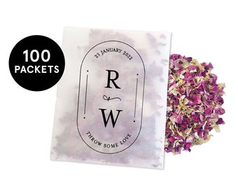 May include: A white packet with the text "100 PACKETS" in a black circle. The packet has a watercolor design with the initials "R" and "W" and the words "THROW SOME LOVE". A pile of dried rose petals is next to the packet.