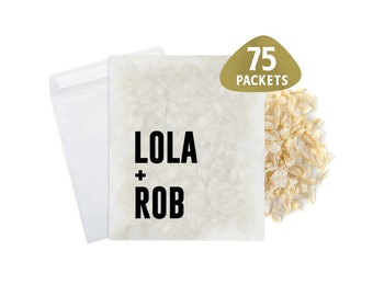 May include: A white paper bag with the text "LOLA + ROB" printed in black. The bag is filled with white paper confetti and a gold sticker with the text "75 PACKETS" is on the right side of the bag.