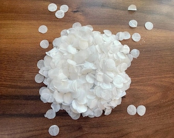May include: A pile of white paper confetti on a brown wooden surface. The confetti is in the shape of small circles.