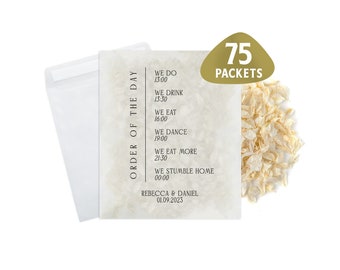 May include: Wedding day order of events card with text "ORDER OF THE DAY" and event times. The card is cream-colored with a textured appearance, and includes the names Rebecca & Daniel and the date 01.09.2023. A gold label reads "75 PACKETS".