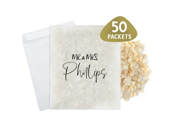 May include: Fifty white paper packets with the text "MR & MRS Phillips" printed on them. The packets are filled with white confetti.