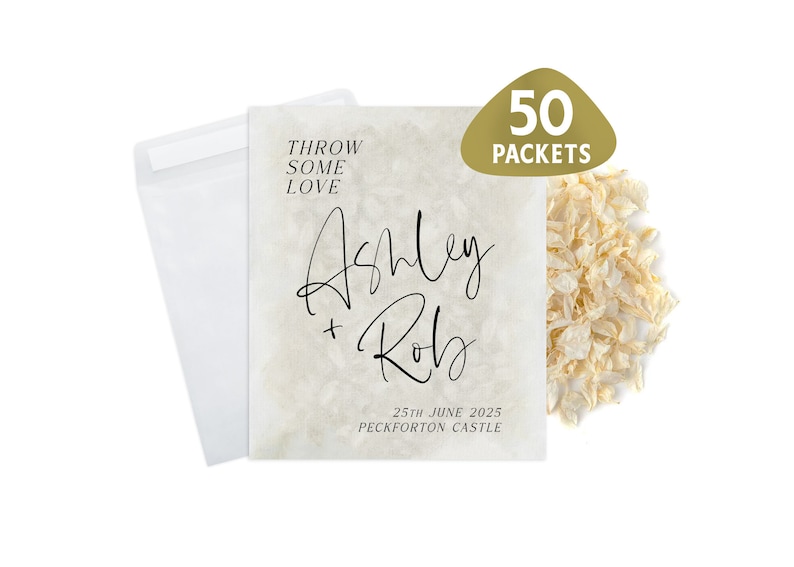 May include: A white envelope with a beige card inside. The card has the text "Throw some love" at the top, followed by the names "Ashley + Rob" in cursive script. The date "25th June 2025" and the location "Peckforton Castle" are printed below the names. A pile of white confetti is in the background.
