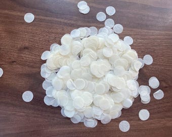 May include: A pile of white paper confetti circles on a brown wooden surface.