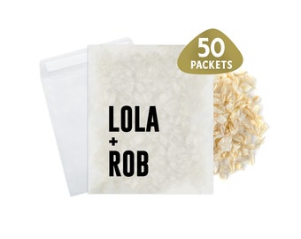 May include: A white paper bag with the text "LOLA + ROB" printed in black. The bag is filled with white paper confetti and a gold sticker with the text "50 PACKETS" is on the right side of the bag.