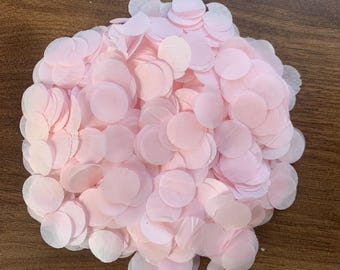 May include: A pile of light pink confetti in a circular shape. The confetti is made of thin, translucent paper and is scattered on a brown wooden surface. The confetti is a pale pink color.