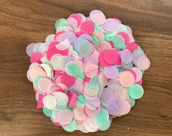May include: A pile of colorful confetti in shades of pink, green, and purple. The confetti is made of thin, round paper pieces, scattered on a wooden surface. The confetti is a mix of light and dark shades.