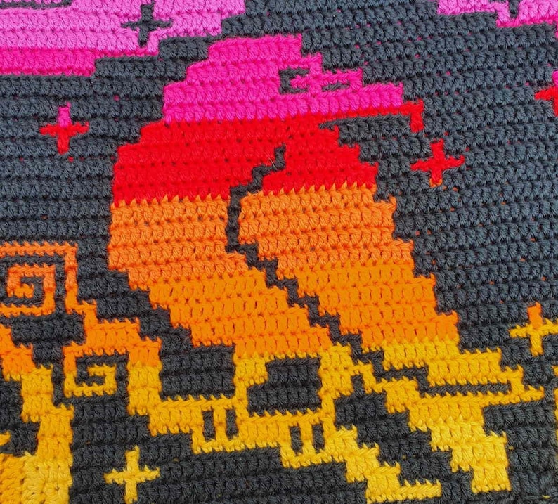 May include: A close-up of a crocheted blanket with a geometric pattern in shades of orange, red, pink, and black.