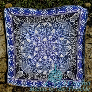 Puede incluir: Una manta de crochet azul y blanca con un patrón geométrico. La manta está hecha con una variedad de puntos y tiene una superficie texturizada. La manta está colocada sobre una superficie de piedra.