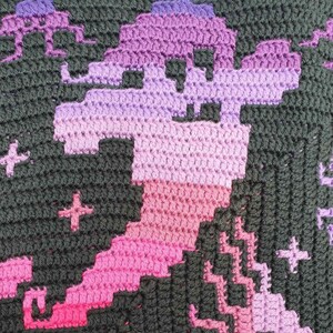 May include: A close-up of a crocheted blanket with a pixelated design of a dragon in shades of pink, purple, and black.
