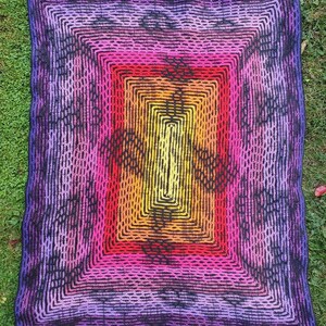 May include: A crocheted blanket with a multi-colored square pattern in shades of purple, pink, orange, yellow, and black. The blanket has a textured, woven look.