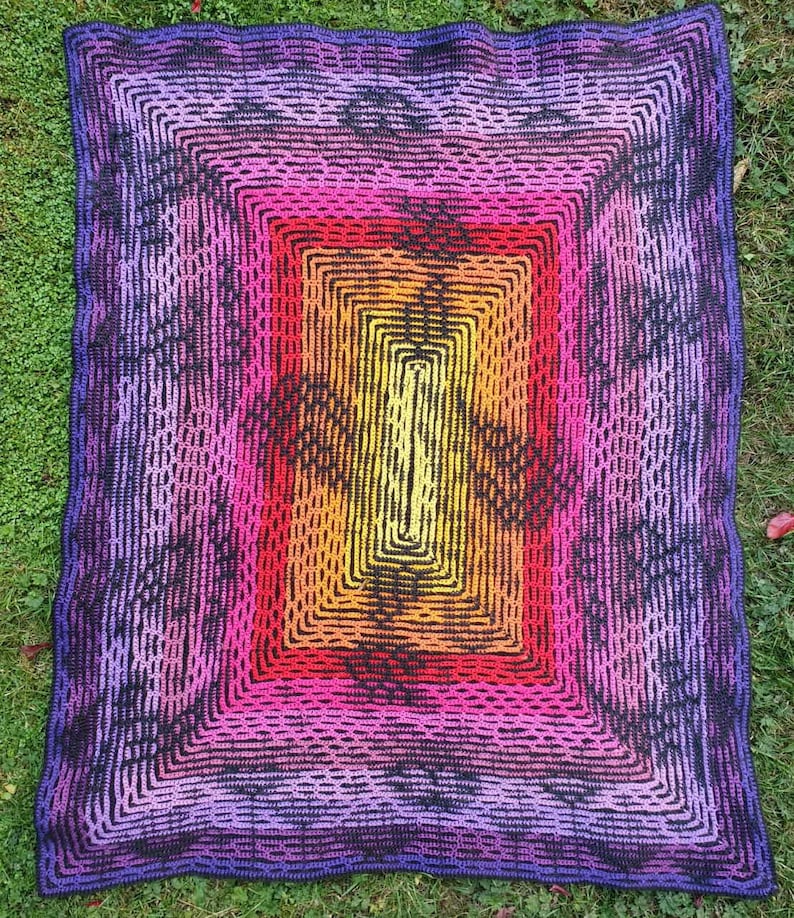 May include: A crocheted blanket with a multi-colored square pattern in shades of purple, pink, orange, yellow, and black. The blanket has a textured, woven look.