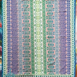 Puede incluir: Una colorida manta de ganchillo hecha a mano con un patrón geométrico. La manta presenta rayas verticales en tonos de azul, verde, rosa y blanco. El borde es de color turquesa sólido. El texto "Ado Crochet" es visible en la esquina inferior izquierda.