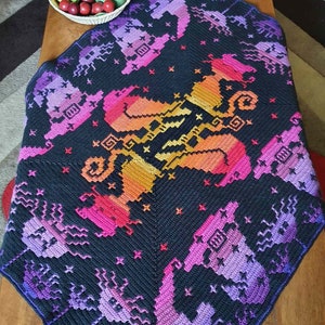May include: A black crochet blanket with a colorful pixelated design of a unicorn. The blanket is made with a variety of shades of purple, pink, orange, and yellow yarn.