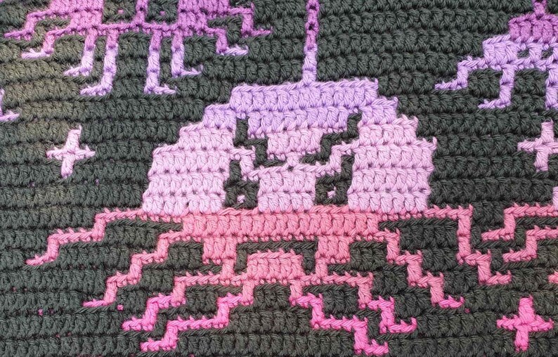 May include: Crocheted blanket with a pink and purple alien design. The alien is surrounded by stars.