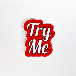 Könnte beinhalten: Roter Aufkleber mit weißem Text, der "Try Me" in einer Retro-Schriftart sagt.