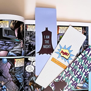 Peut inclure: Pages de bande dessinée et plusieurs marque-pages. L'un présente une silhouette de Batman avec le texte "I AM THE NIGHT". Un autre affiche un graphique "POW!" et "To be continued". Le troisième a un motif "HAHAHA".