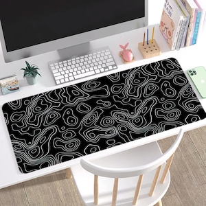 May include: A black and white desk mat with a topographic pattern. The mat is on a white desk with a computer, keyboard, and other office supplies.