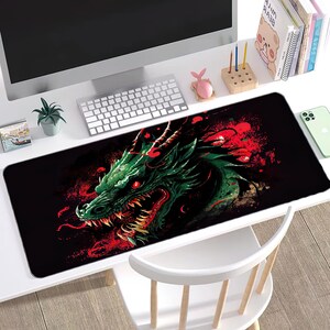 Puede incluir: Un ratón de ordenador negro y verde con un dragón y salpicaduras de pintura roja. El dragón está mirando hacia el lado izquierdo de la imagen y tiene una expresión feroz.