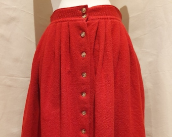 Puede incluir: Una falda midi roja con cierre de botones en la parte delantera. La falda está hecha de una tela texturizada y tiene una silueta ligeramente acampanada.