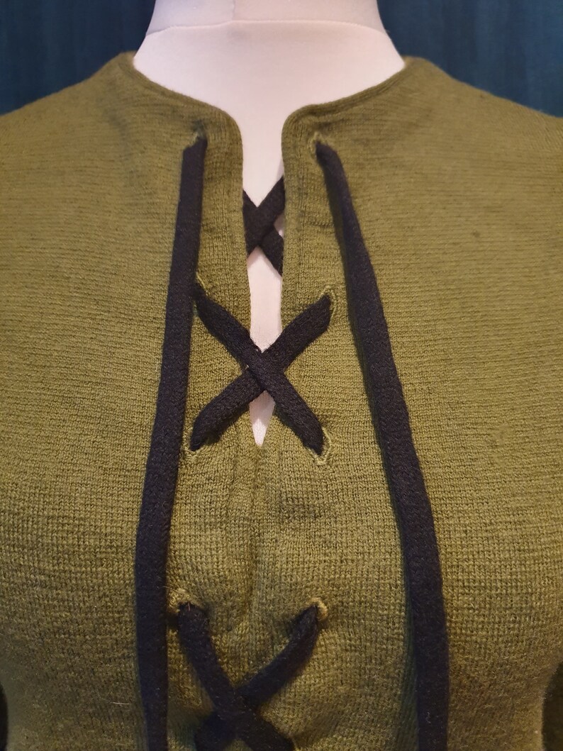Op de afbeelding: Een groene trui met een zwarte veterkraag.