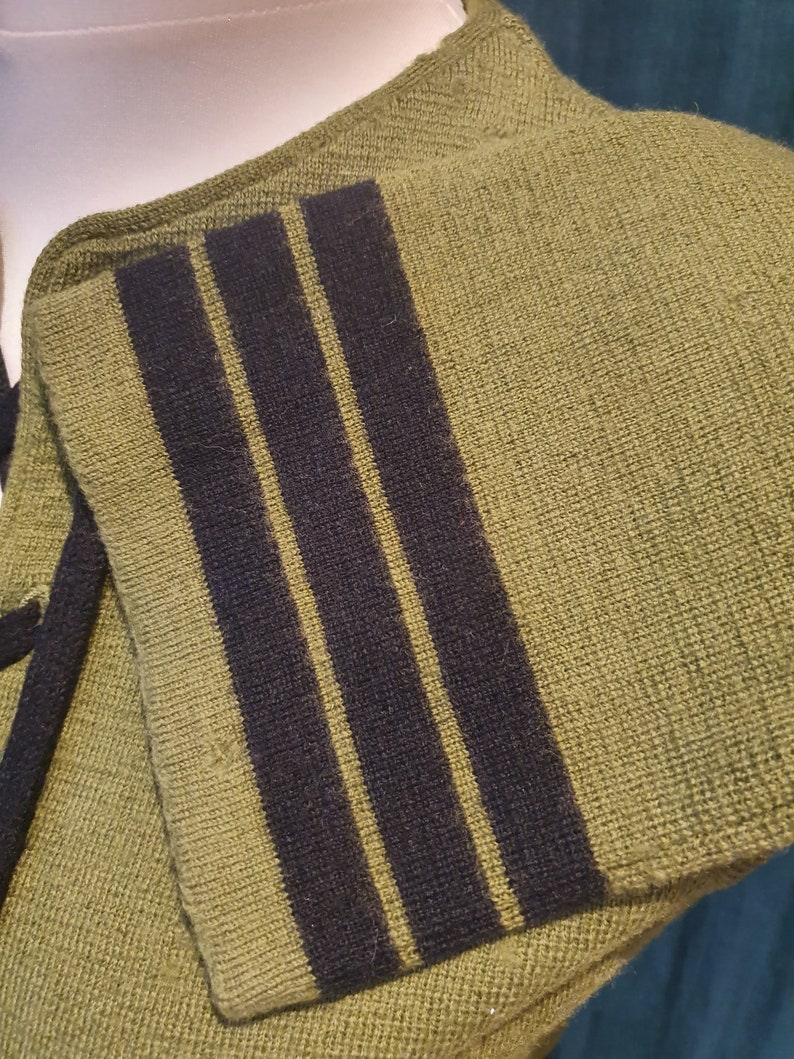 Op de afbeelding: Een groene gebreide trui met zwarte en gele strepen op de mouw.