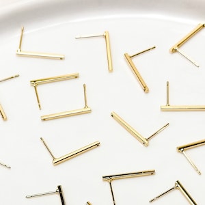 May include: A white plate with a collection of gold bar earrings. The earrings are in various positions, some are straight and some are angled.