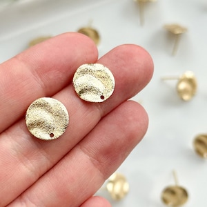 Puede incluir: Dos discos redondos de metal dorado con una superficie texturizada y un pequeño agujero en el centro. Los discos están sobre una superficie blanca.
