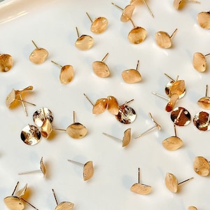 May include: A white tray filled with gold-toned earring findings. The findings are small, round, and have a post on the back.