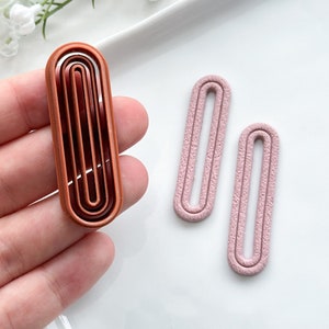 May include: Two pairs of earrings, one pair is brown with a multi-layered design and the other pair is pink with a simple design.