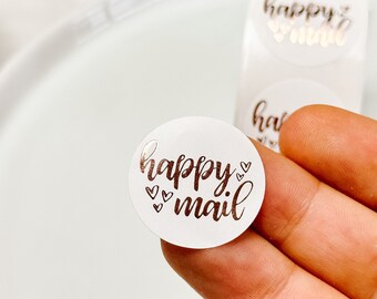 May include: Round white sticker with the text "happy mail" in gold script with small hearts around the text.