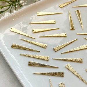 Pode incluir: Uma coleção de formas triangulares de metal dourado com uma superfície texturizada. As formas estão dispostas em um prato branco.