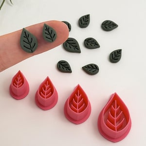 Puede incluir: Una colección de herramientas y recortes en forma de hoja. La imagen muestra varios pequeños recortes de hojas de color verde oscuro y tres herramientas rosas en forma de hoja. Las herramientas tienen un diseño de vena de hoja.