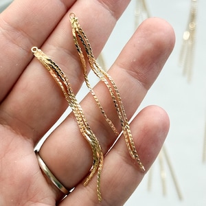 Op de afbeelding: Goudkleurige oorbellen met een gelaagd kettingontwerp. De oorbellen hebben een delicate, vloeiende uitstraling, met meerdere strengen fijne kettingen die een golvend effect creëren. De oorbellen worden getoond tegen een witte achtergrond.