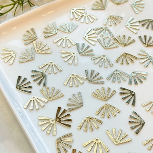 Peut inclure: Un plateau blanc rempli d'embellissements en métal doré en forme d'éventail. Les embellissements ont une surface texturée et sont disposés de manière aléatoire.