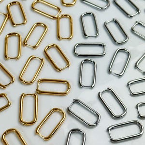 Peut inclure: Une collection de nombreuses petites boucles d'oreilles créoles rectangulaires dispersées dans le cadre. Les boucles d'oreilles sont en métal poli et sont disponibles en finitions dorées et argentées, avec un mécanisme de fermeture à charnière.