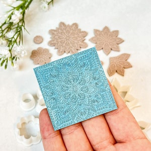 Op de afbeelding: Een blauwe siliconen cakedecoratievorm met een gedetailleerd mandala-ontwerp. De vorm wordt in een hand gehouden. Er zijn andere cakedecoratiegereedschappen op de achtergrond.