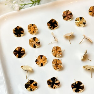 May include: A collection of gold-toned metal earring studs with a ruffled, textured design. The earrings are displayed on a white surface.