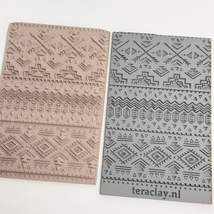 May include: Two rectangular clay stamps with geometric patterns. One is a light brown color, and the other is gray. The stamps feature repeating designs of triangles, diamonds, and lines. The gray stamp has the text "teraclay.nl" on it.