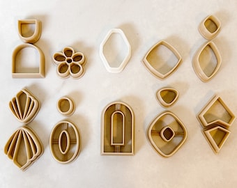 May include: A set of 11 cookie cutters in various geometric shapes, including arches, diamonds, ovals, and a flower. The cutters are made of a beige plastic material.