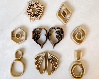 May include: A set of ten cookie cutters in various shapes, including a sunflower, a heart, a diamond, a circle, and a leaf. The cutters are made of a beige plastic material.
