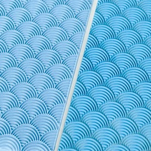 Pode incluir: Dois tapetes de textura retangulares de silicone azul-claro com um padrão em relevo repetitivo de semicírculos sobrepostos. As folhas flexíveis exibem um design ondulado consistente em toda a superfície, criando uma grade uniforme de arcos.